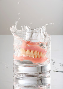 Artificial Teeth or Dentures Dropping into a Glass of Water